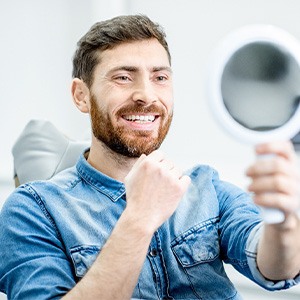 man smiling and looking in a mirror after getting his restorations for dental implants