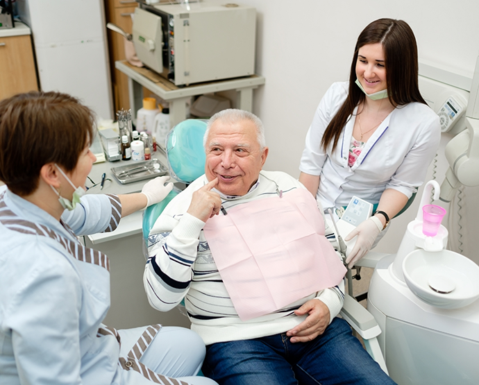 Senior male patient talking to two female dentists