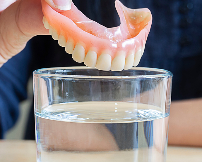 Close up of dentures being placed in glass of water