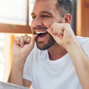 Man smiling while flossing his teeth in bathroom