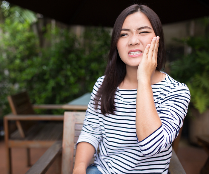 Woman in striped shirt rubbing jaw in pain