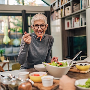 Woman with black glasses smiling while eating with friend