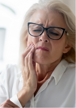 Woman with glasses rubbing jaw in pain