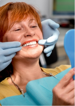 Female dental patient checking smile in handheld mirror