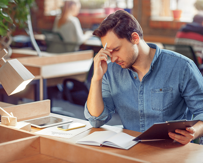 Man in denim shirt looking at books and feeling tired