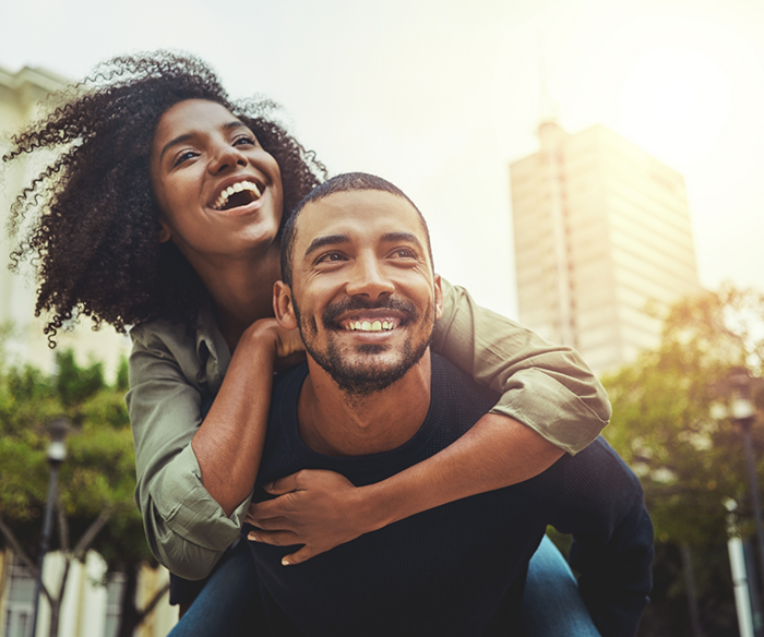 Man giving woman piggyback ride while outside in city